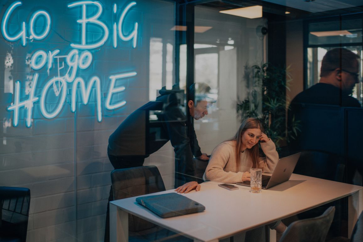 Blick durch Glaswände in ein modernes Büro mit Besprechungsraum und arbeitenden Personen im Hintergrund