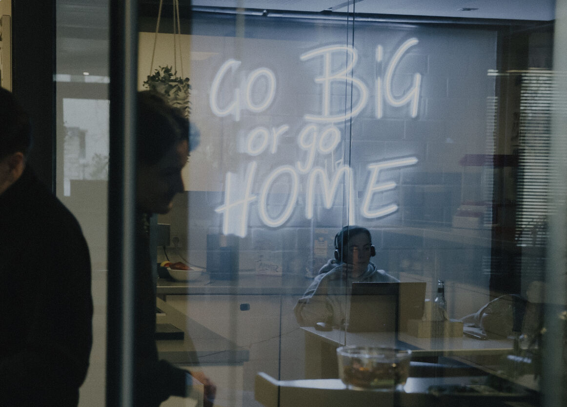 Blick durch eine Glaswand in einen Besprechungsraum mit der Aufschrift 'Go Big or Go Home'