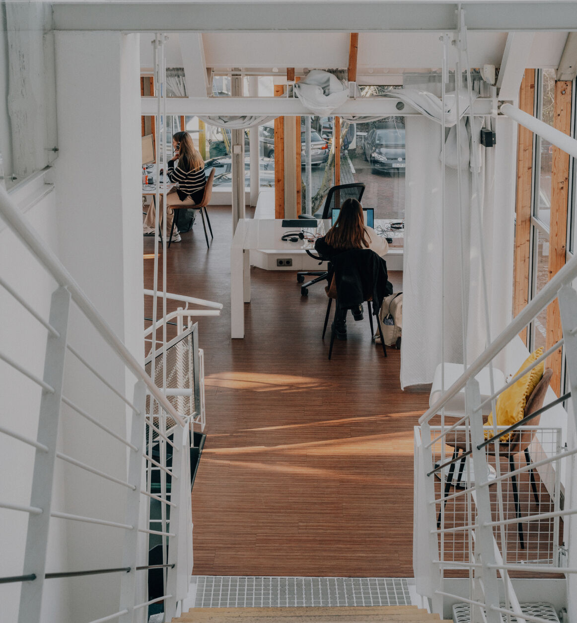 Blick von einer Treppe in ein helles, modernes Büro mit Holzfußboden und Glasfronten