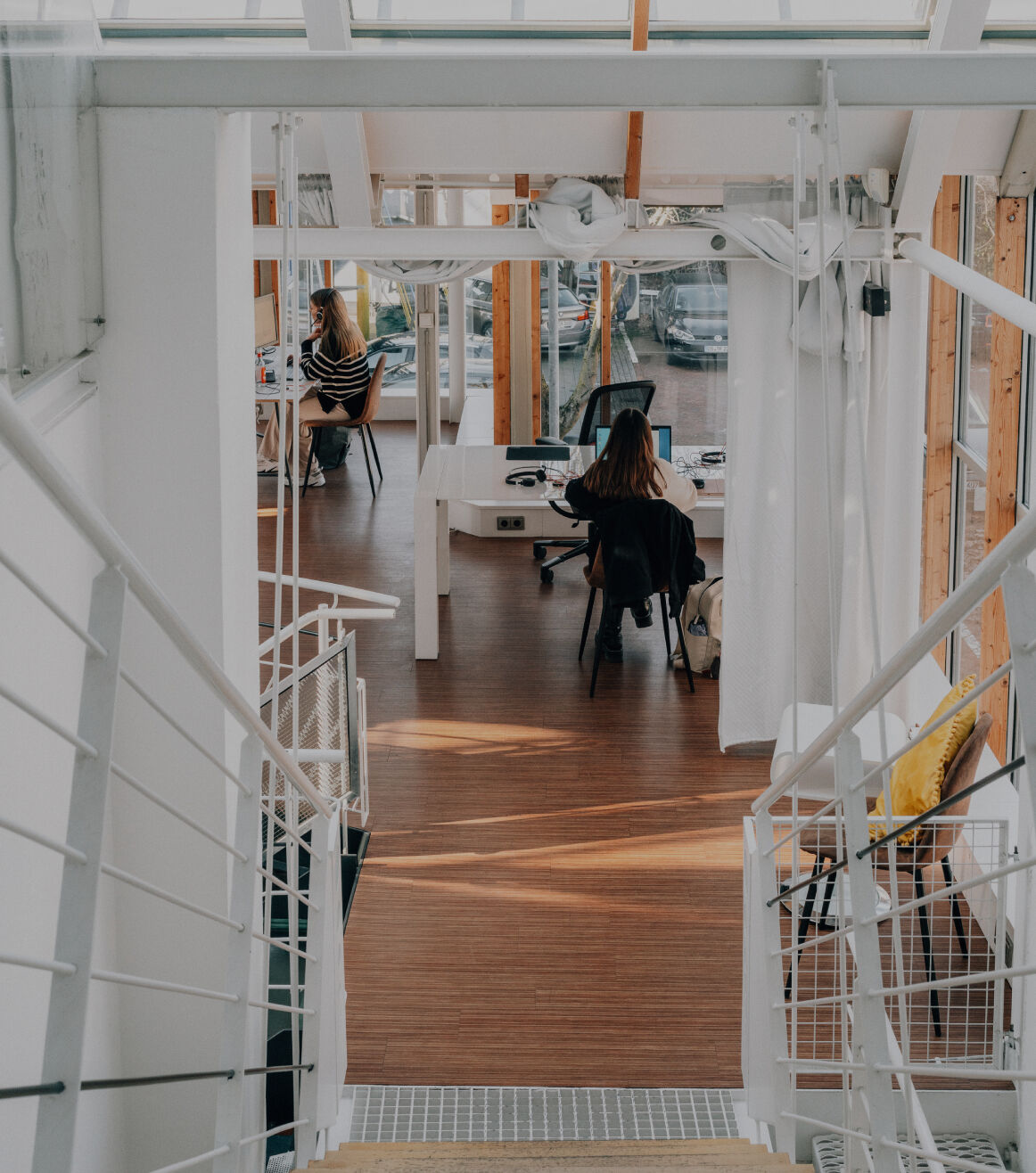 Helles modernes Büro mit Glasfronten, in dem zwei Personen an Schreibtischen arbeiten