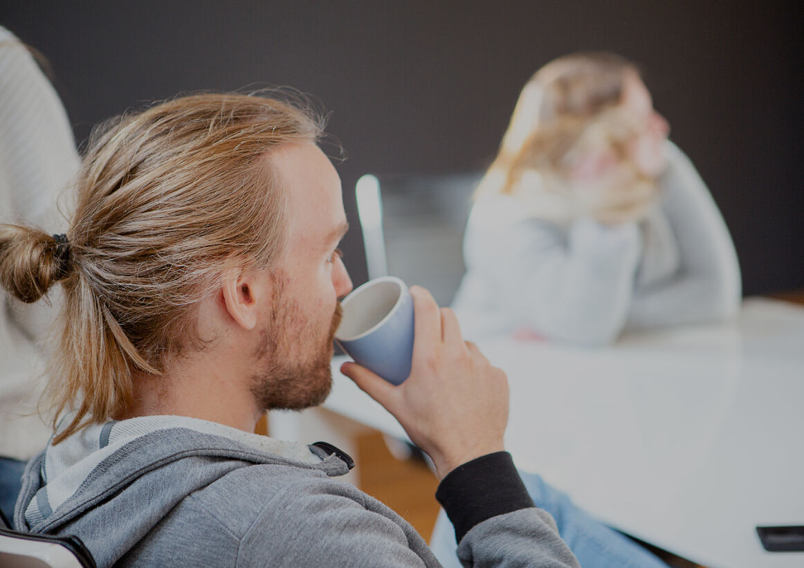 Person mit zusammengebundenem Haar trinkt aus einer Tasse in einem hellen Besprechungsraum