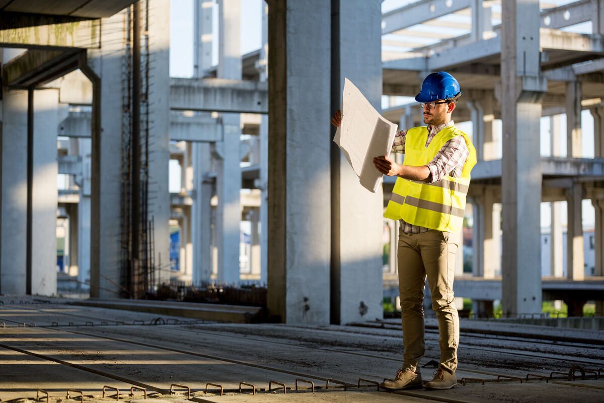 Bauleiter mit Plänen und Warnweste im Rohbau