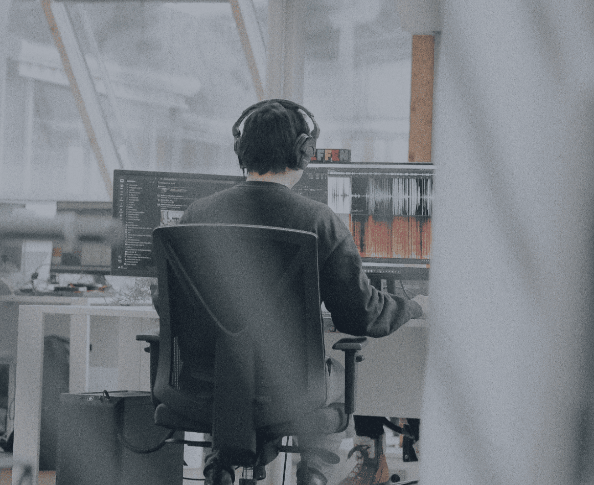 Person mit Kopfhörern arbeitet an einem Laptop im Büro, von hinten aufgenommen.
