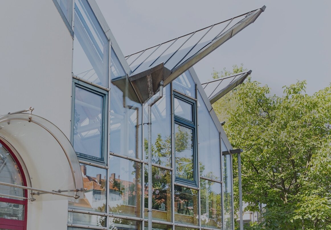 Außenansicht eines modernen Bürogebäudes mit Glasfassade, großen Fenstern und Bäumen im Vordergrund.
