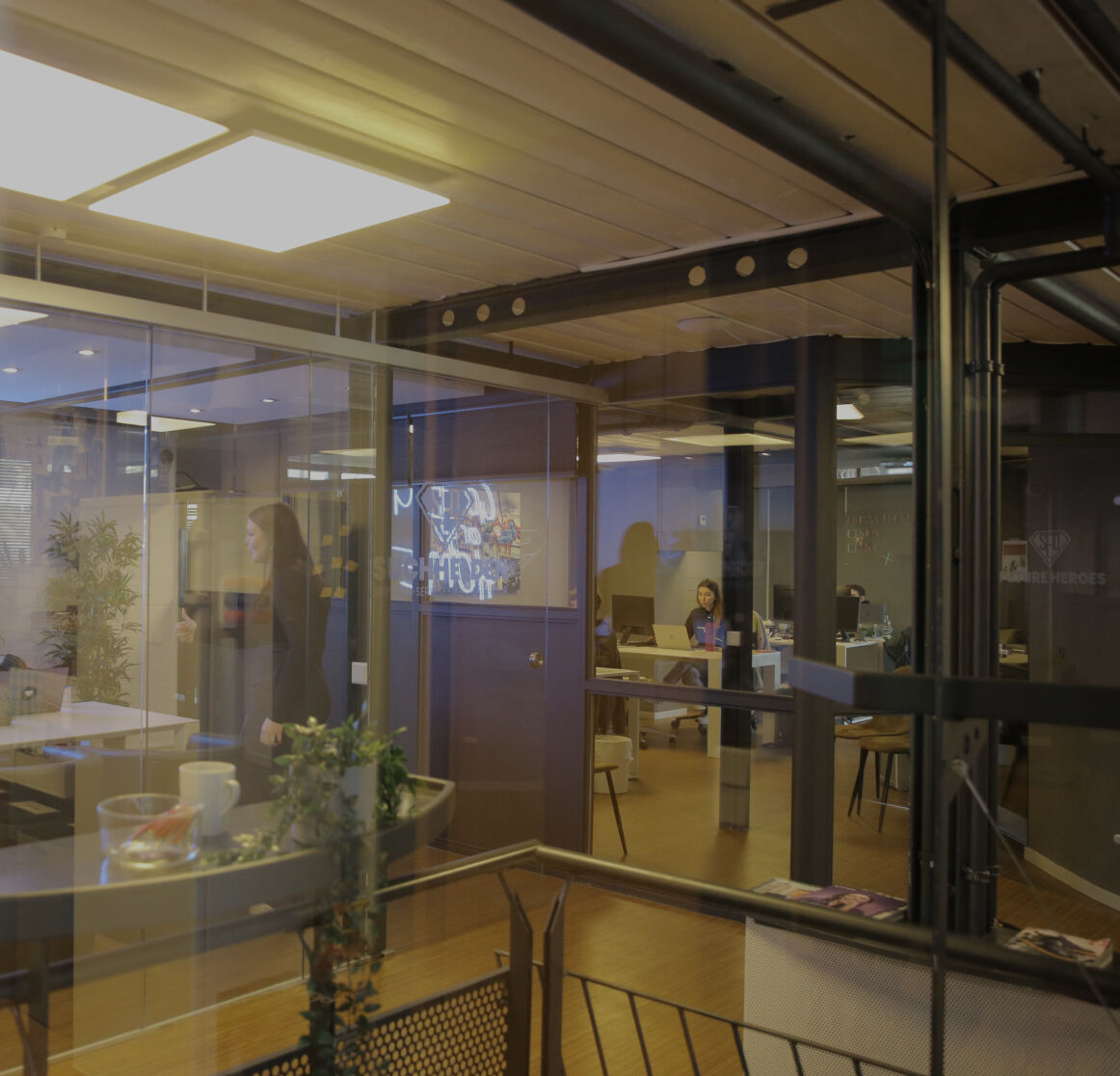 Blick durch Glaswände in ein modernes Büro mit Besprechungsraum und arbeitenden Personen im Hintergrund