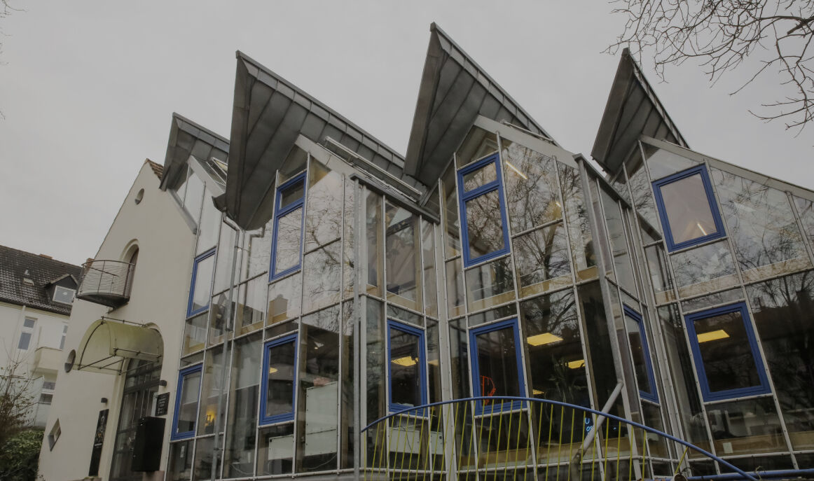 Aussenansicht eines modernen Glasgebäudes mit blauen Fensterrahmen und schrägem Dach