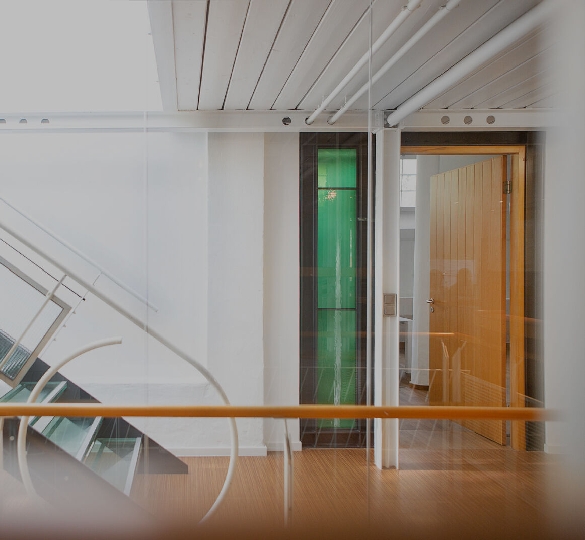 Heller Büroflur mit moderner Glas- und Metalltreppe, weißen Wänden und Holzboden